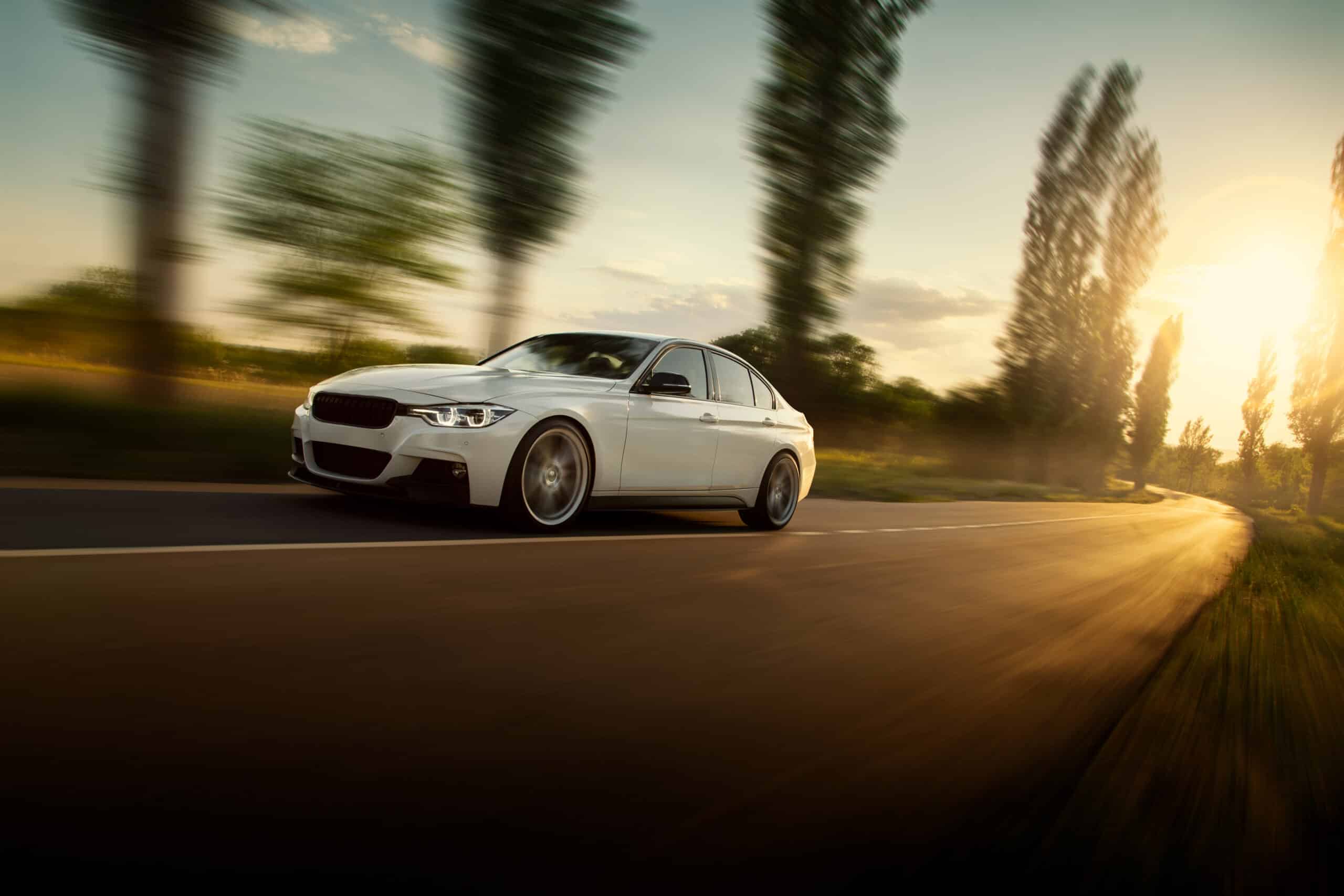 BMW Série 3 blanche en mouvement rapide sur route sinueuse au coucher du soleil, effet filé.